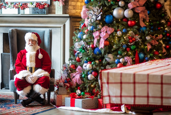 santa claus seated next to a lavishly decorated christmas tree in the elegant surroundings of pivot hotels.