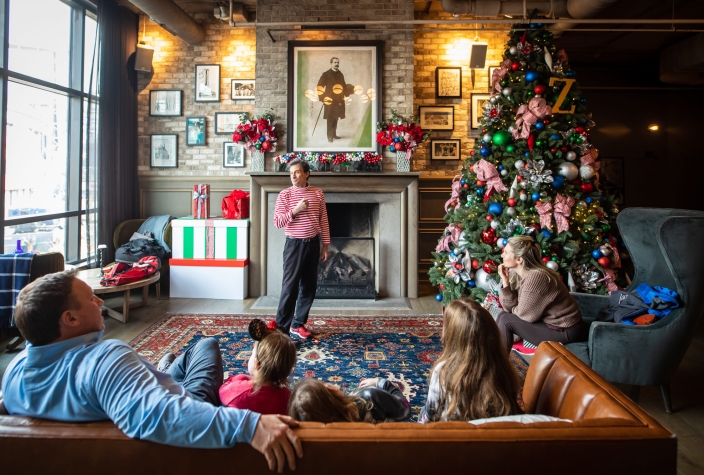 family enjoying a game of charades in a festively decorated living room at pivot hotels during the christmas holidays.