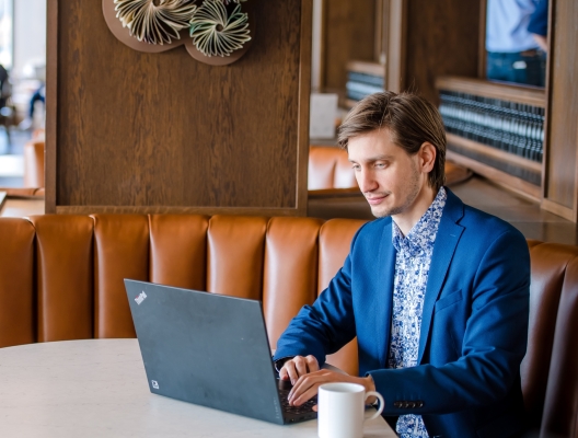 seated man at a booth table works on a laptop computer