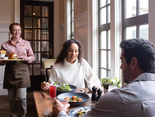 A woman an man dining at a table. The server is delivering their main meal