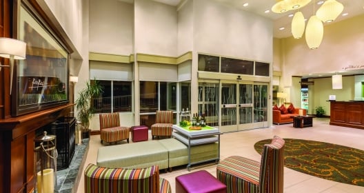 The lobby of the Hilton Garden Inn Arlington hotel with a large fireplace and colorful furniture.