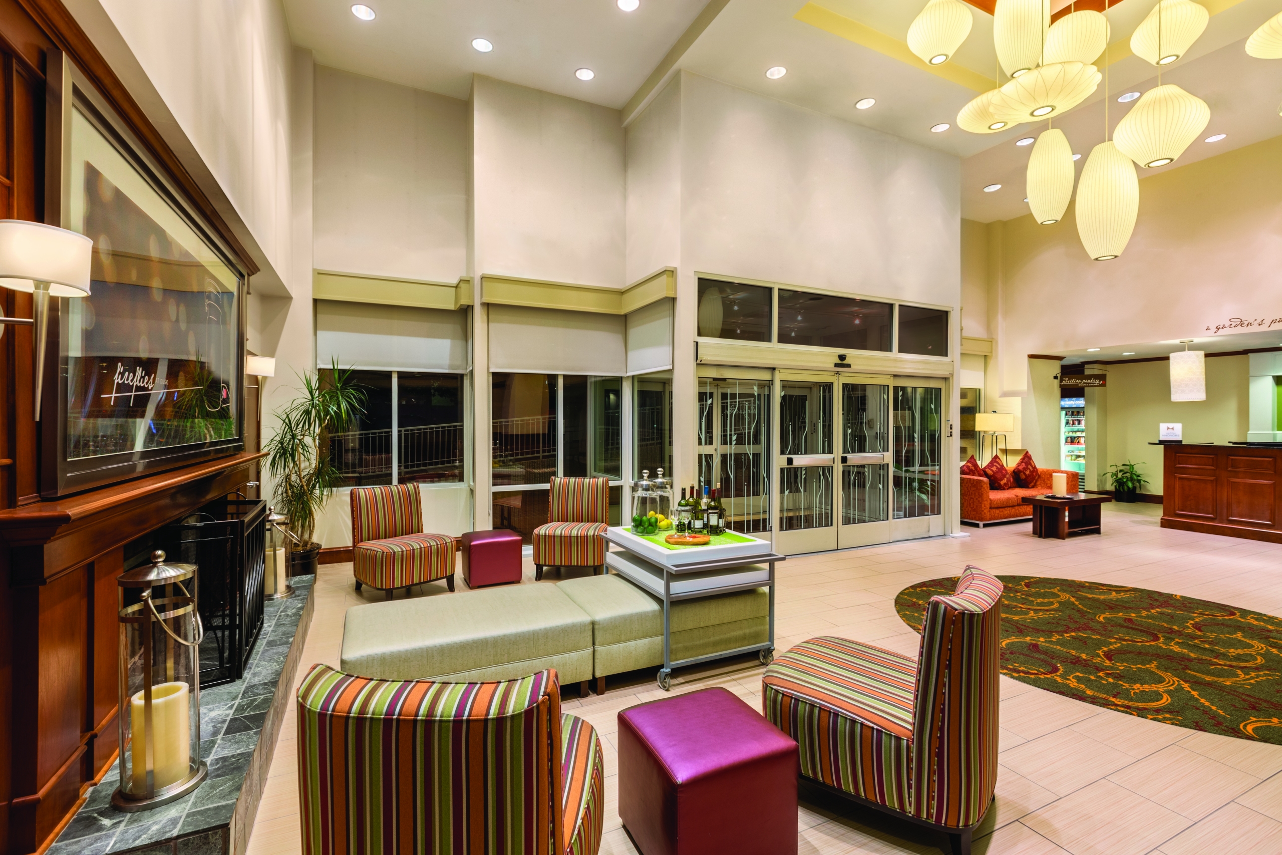 The lobby of the Hilton Garden Inn Arlington hotel with a large fireplace and colorful furniture.