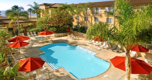 The pool area at the Hilton Garden Inn Carlsbad Beach hotel with lounge chairs and red umbrellas.