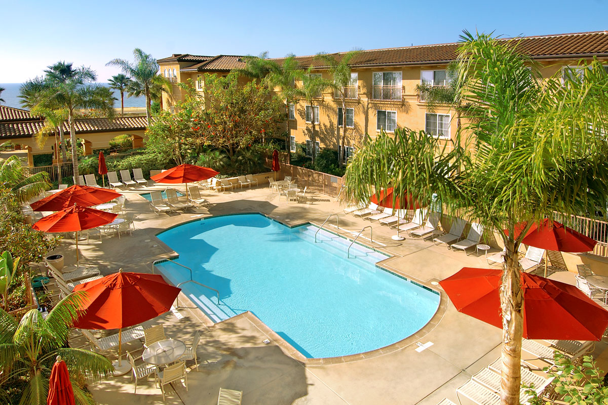 The pool area at the Hilton Garden Inn Carlsbad Beach hotel with lounge chairs and red umbrellas.