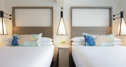 Two side-by-side hotel beds with colorful pillows and a nightstand between them