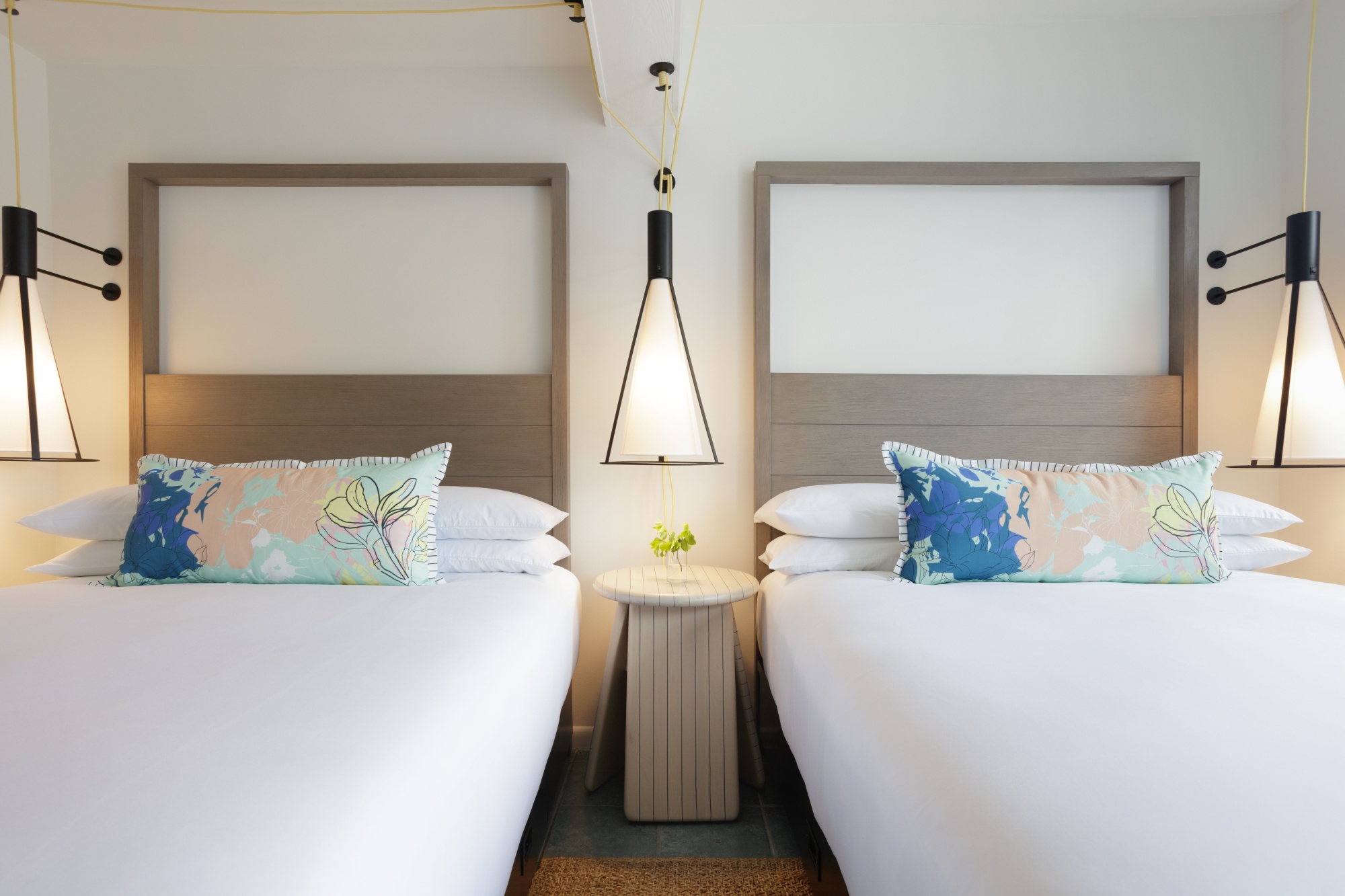 Two side-by-side hotel beds with colorful pillows and a nightstand between them