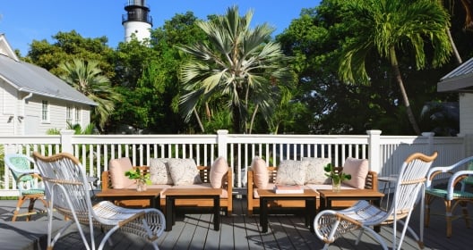 An outdoor patio with wicker furniture. In the background there are palm trees and a lighthouse