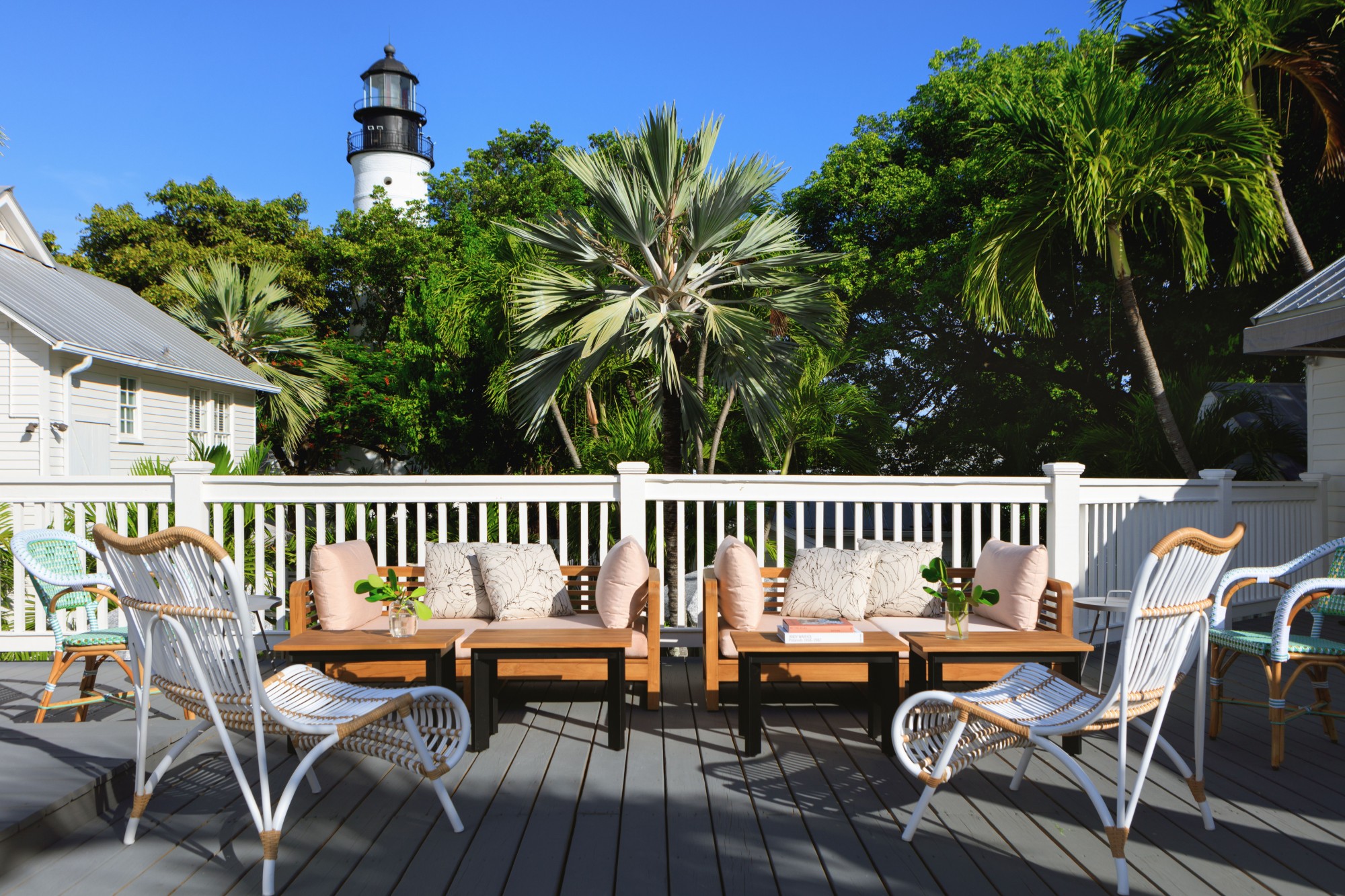 An outdoor patio with wicker furniture. In the background there are palm trees and a lighthouse