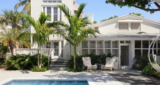 A spacious pool area with wicker pool chairs and palmtrees