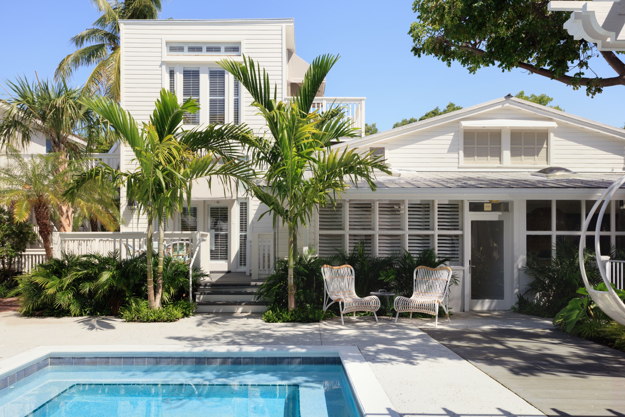 A spacious pool area with wicker pool chairs and palmtrees